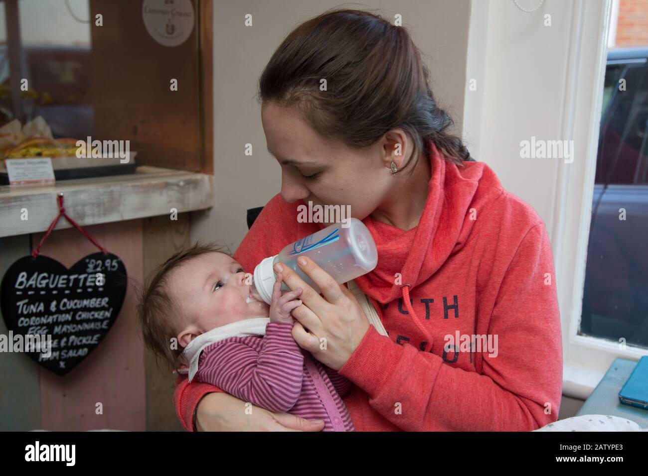 A young mum bottle feeding her 4 month old baby in a cafe, UK Stock Photo