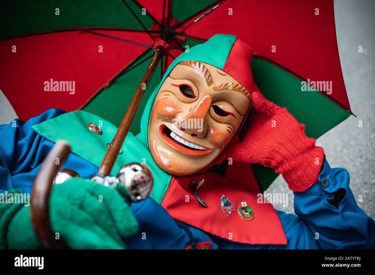 Oberwindemer Spitzbue - Carnival fool in red-green robe and umbrella rests on the floor. During the carnival parade in Staufen, southern Germany. Stock Photo