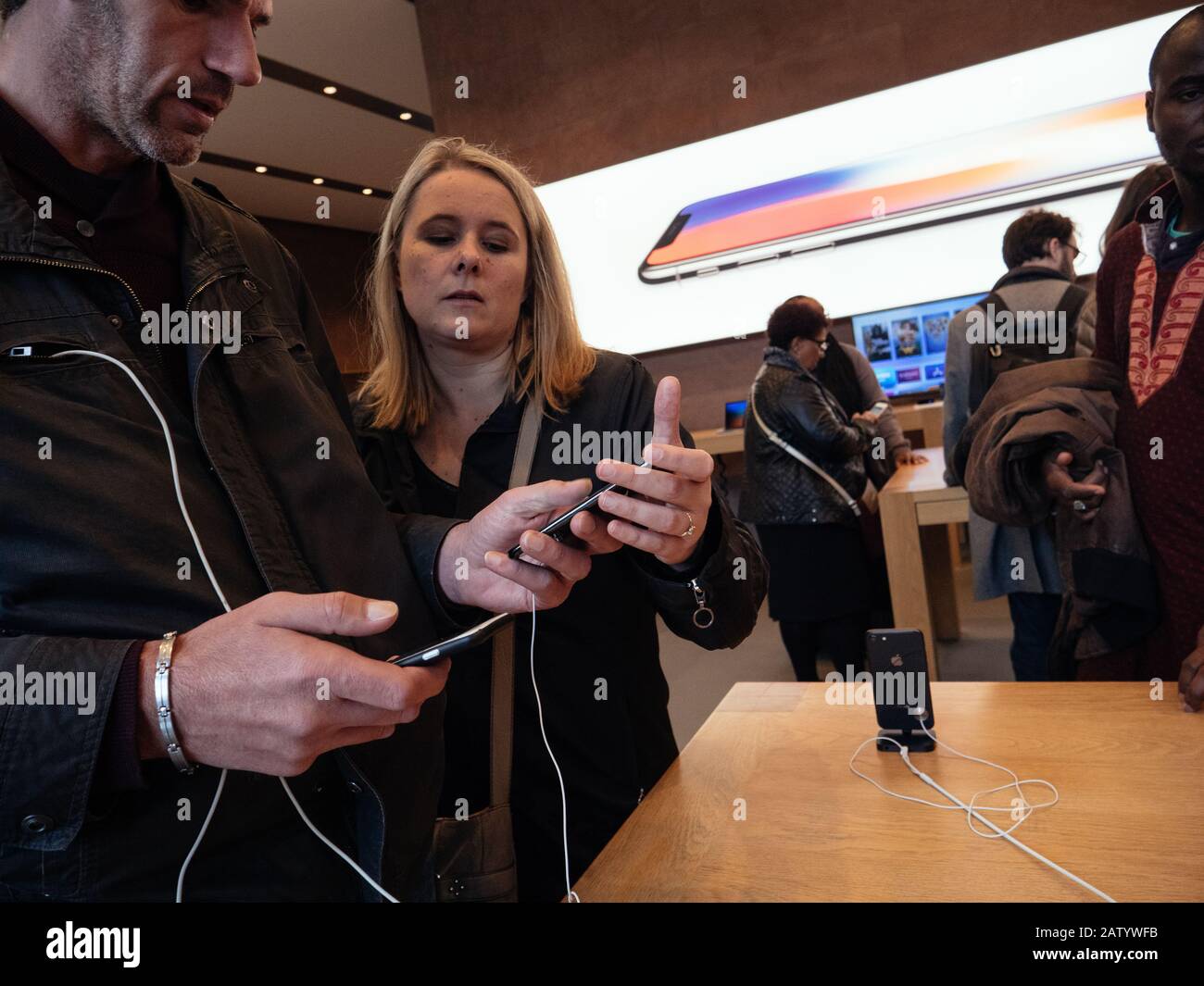 Paris, France - Nov 3, 2017: Side view of young couple admiring inside Apple Store the latest professional iPhone smartphone manufactured by Apple Computers comparing with older model Android phone Stock Photo