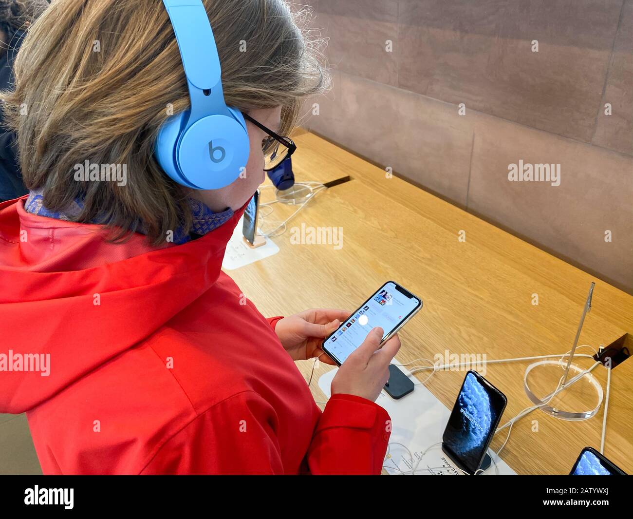Paris, France - Nov 02, 2019: Side view woman in red coat inside Apple Computers Store testing listening to music with new latest Beats by Dr Dre Solo Pro Active Noise Cancelling headphones Stock Photo