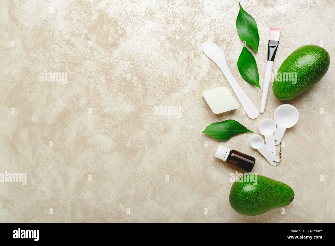 Cosmetology set for cooking, applying face mask. Avocado face mask, spatula, brush, measuring spoons, essential oil on light pink background with copy Stock Photo