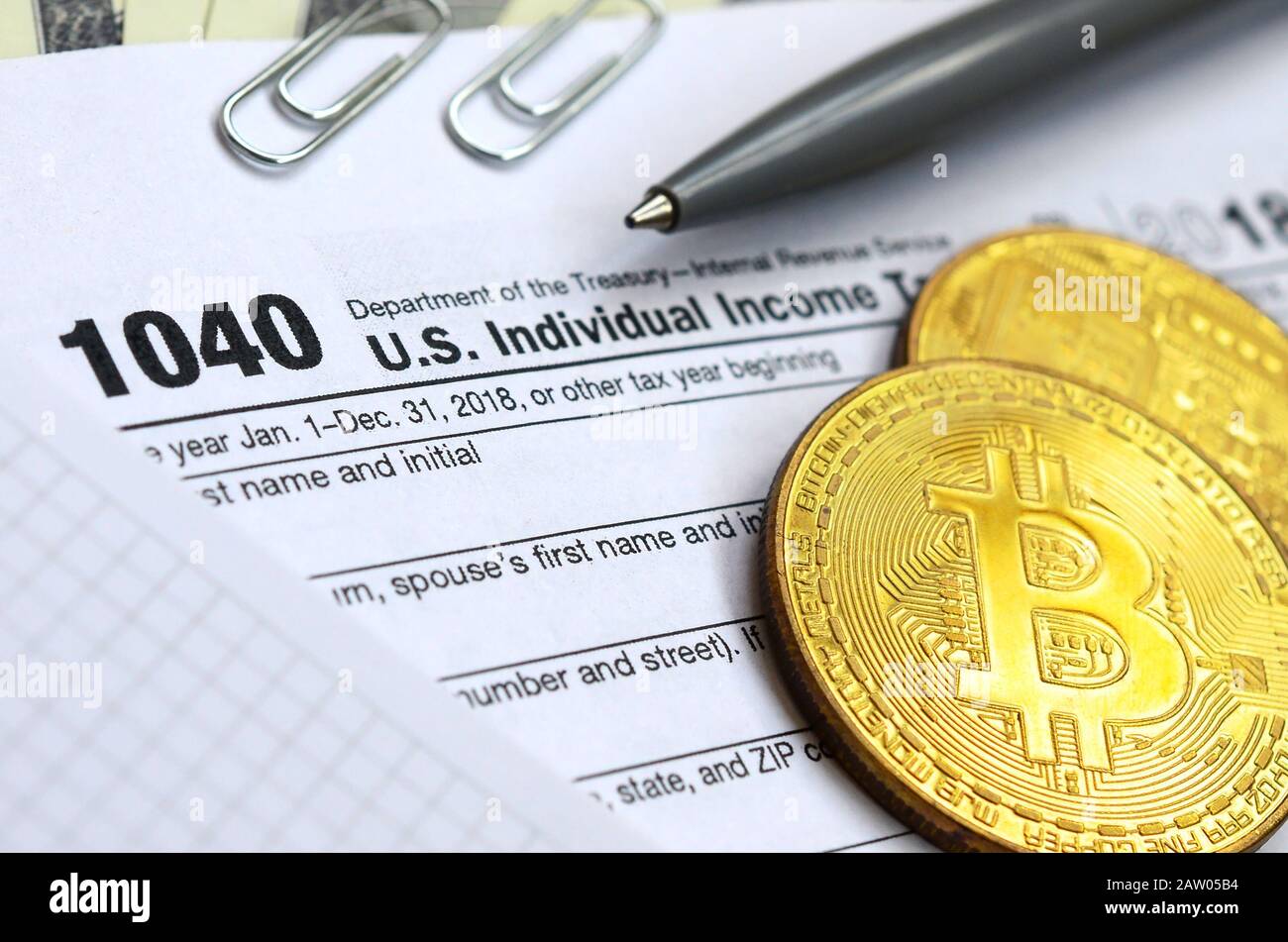 The pen, bitcoins and dollar bills is lies on the tax form 1040 U.S