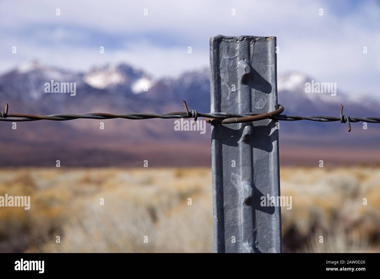 detail of barbed wire fence on metal post with selective focus and defocussed mountains in the distance Stock Photo