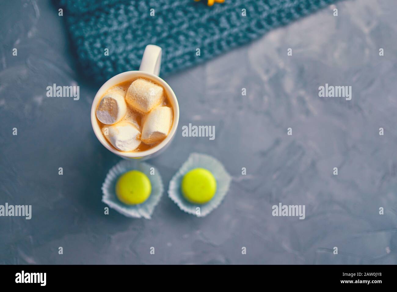 Hot coffee with marshmallow and milk or cream and yellow macaroons on the loft table in a romantic setting with chrysanthemums nearby Stock Photo