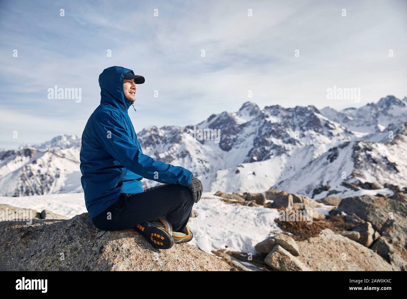Portrait of happy Asian climber in blue jacket at high snowy mountains at background. Outdoor climbing and mountaineering concept. Stock Photo