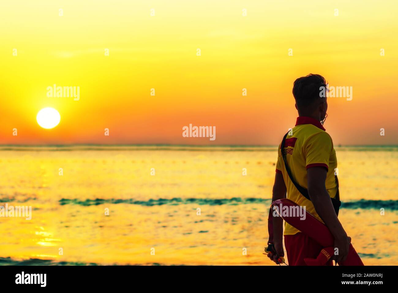 A beach lifeguard dressed in yellow-red uniform at the seaside during sunset in a beach of Dubai in the United Arab Emirates. Stock Photo