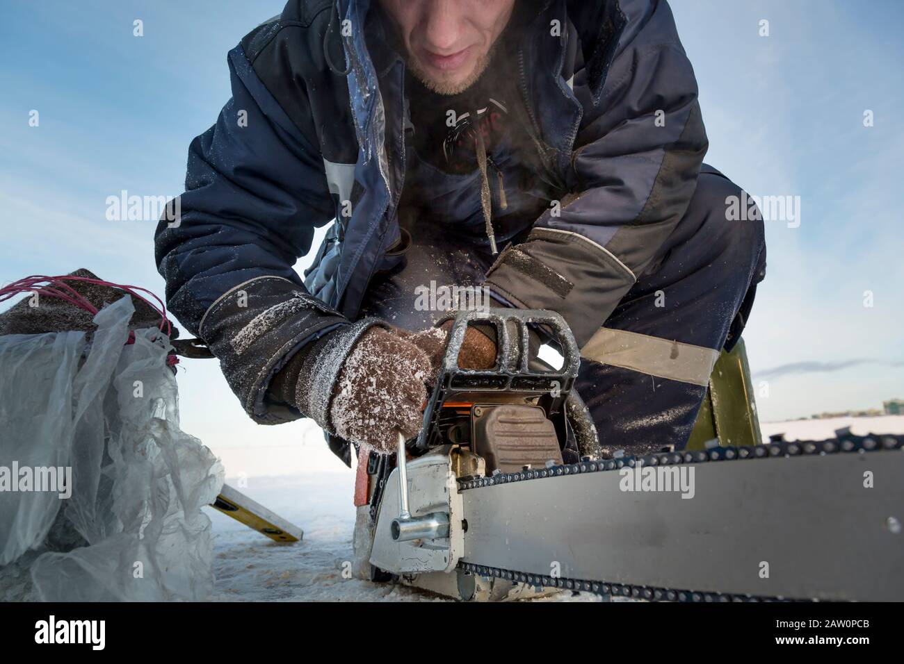 A worker in a blue jacket sharpens a chainsaw chain. Stock Photo