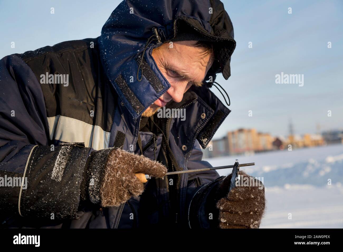 A worker in a blue jacket sharpens a chainsaw chain. Stock Photo