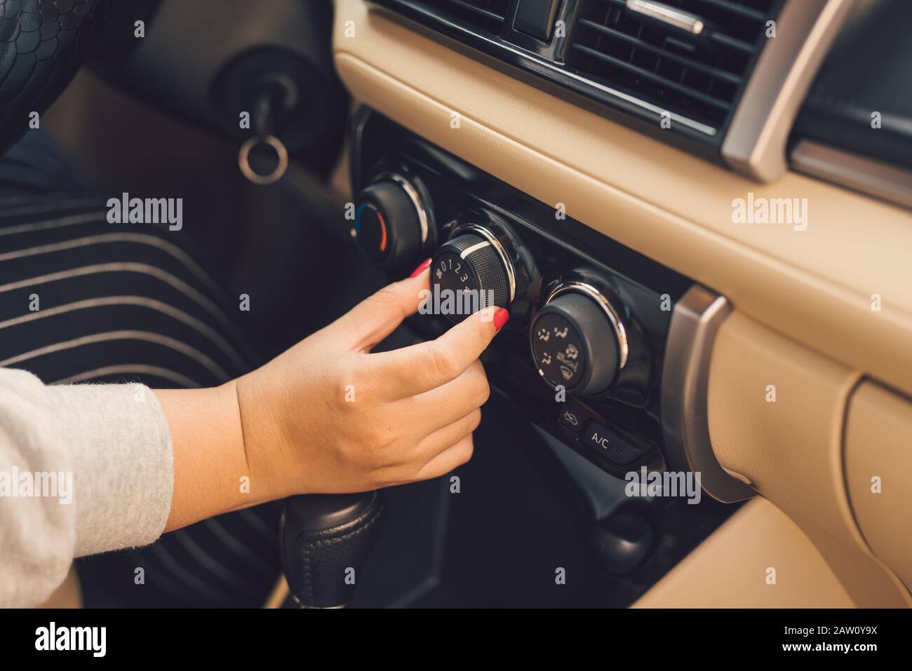 Hand of woman turning on car air conditioning system,Button on dashboard in car panel Stock Photo