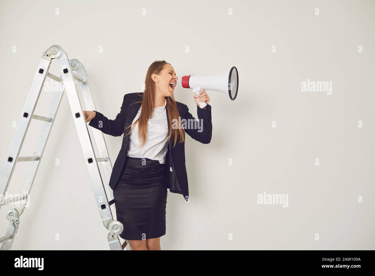 Businesswoman on the stairs with a megaphone in hand shouts on a gray background. Stock Photo
