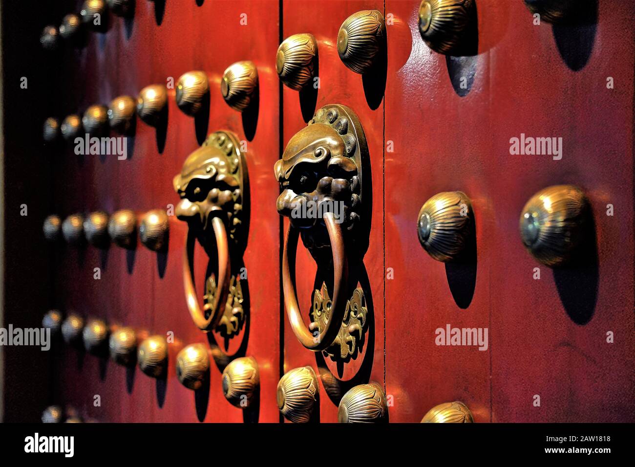 Pair of bronze Chinese Lion head door knockers on red Buddhist temple door in Chinatown Singapore in evening light and perspective view and soft focus Stock Photo