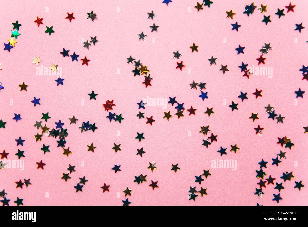 Multicolored confetti or sparkles in the form of small stars on a pink background. Celebration of the holiday. Stock Photo