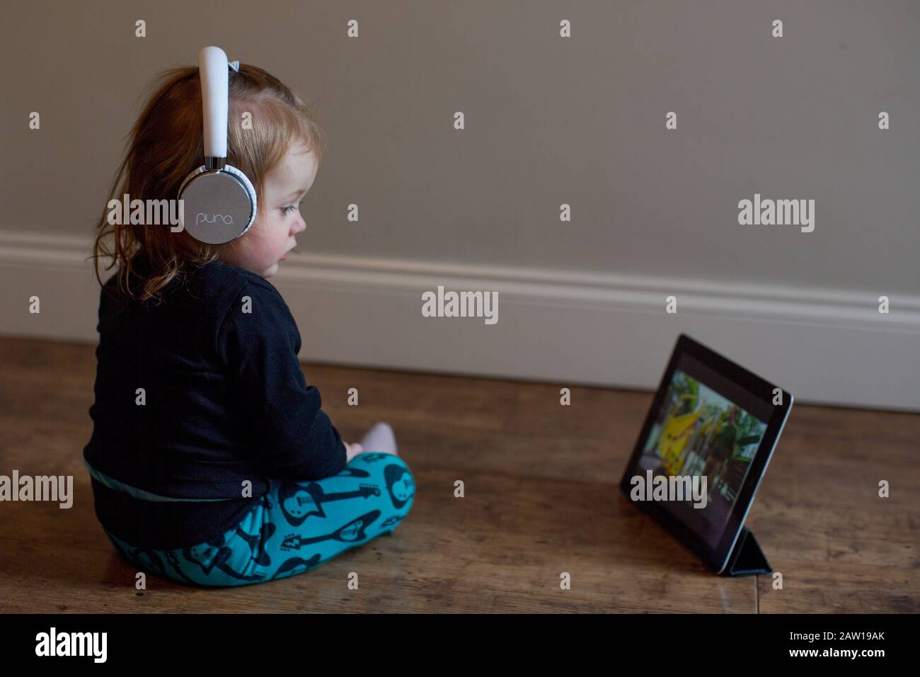 15 month old girl wearing headphones and watching a film on an iPad, UK Stock Photo Alamy