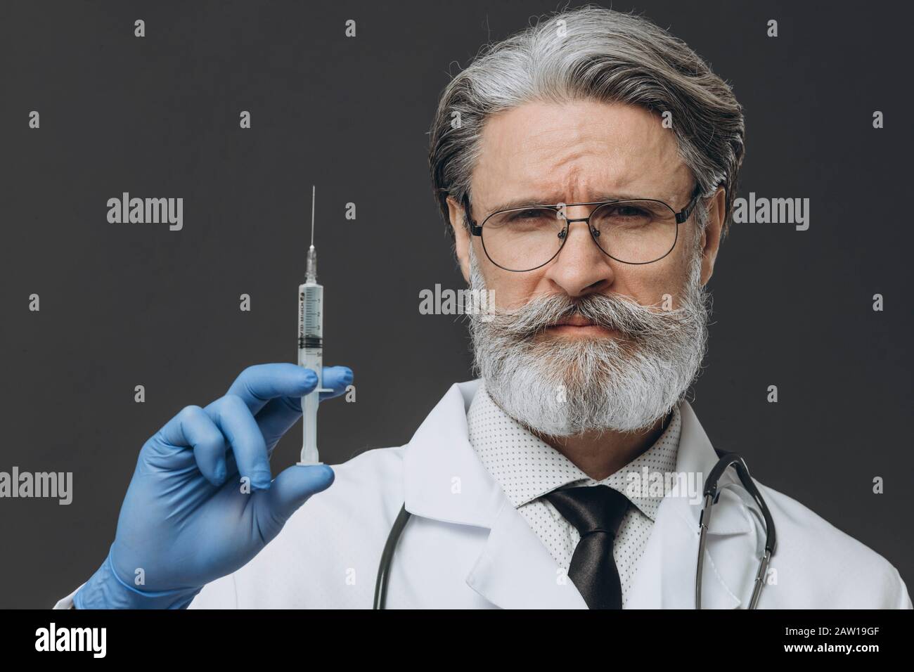 Old serious doctor holding syringe with vaccine. Ready to make injection. Stock Photo