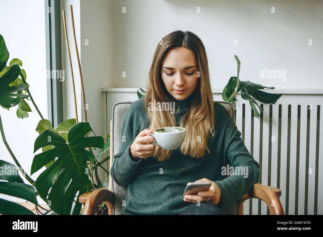 Girl drinks a hot morning drink and uses a cell phone. Stock Photo