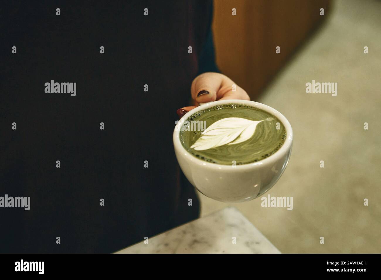 Barista holds a fragrant and healthy matcha latte tea in her hands. Stock Photo