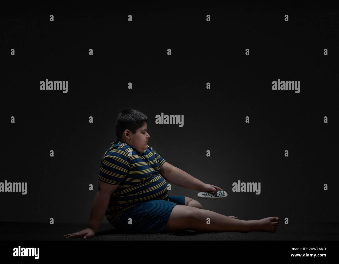 Young boy sitting on the floor and changing channels with the TV remote. (Obesity) Stock Photo