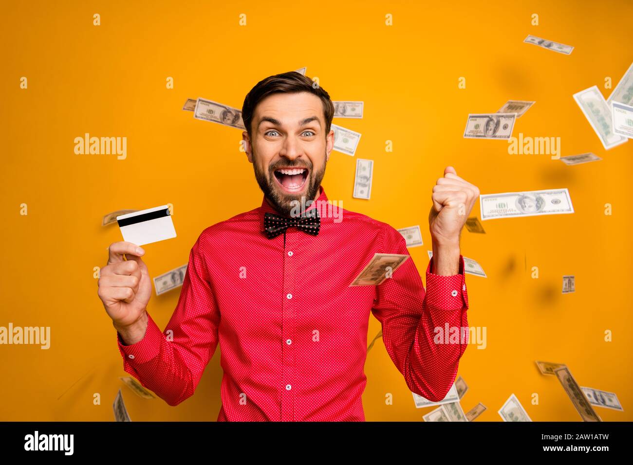 Photo of attractive funny guy hold plastic credit card rich person money bucks falling everywhere screaming wear trendy red shirt bow tie clothes Stock Photo