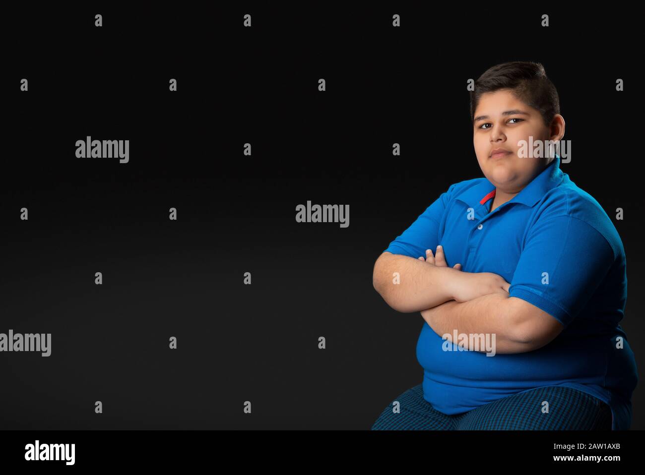 Young boy sitting with his hands folded on his chest. (Obesity) Stock Photo