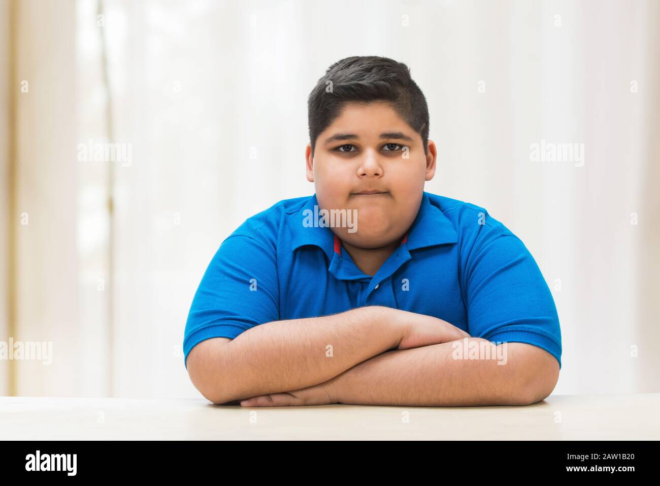 Portrait of a chubby boy sitting with his hands on the table. (Obesity) Stock Photo