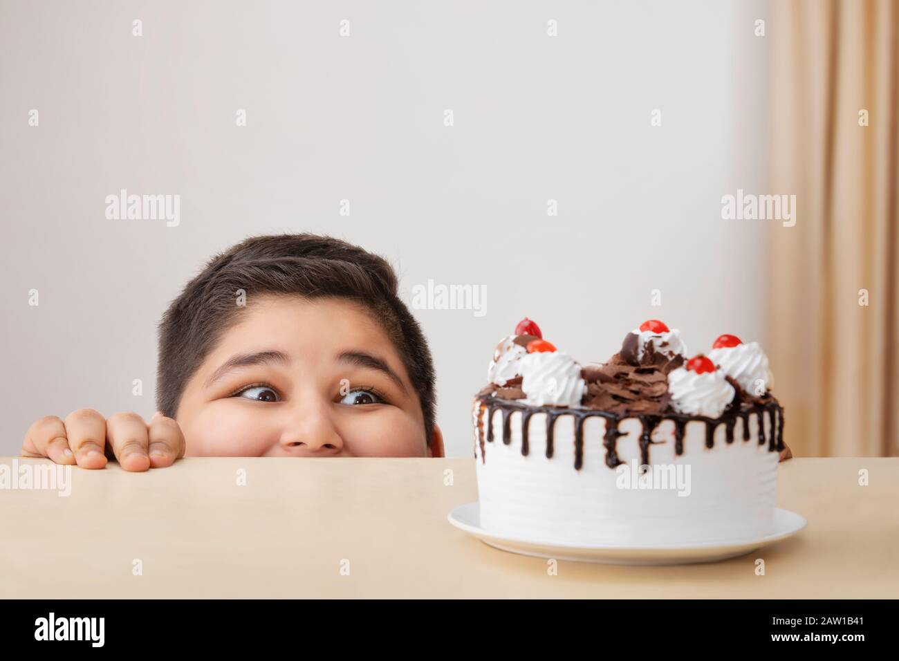 Young boy looking hungrily at a cake kept on the table. (Obesity) Stock Photo