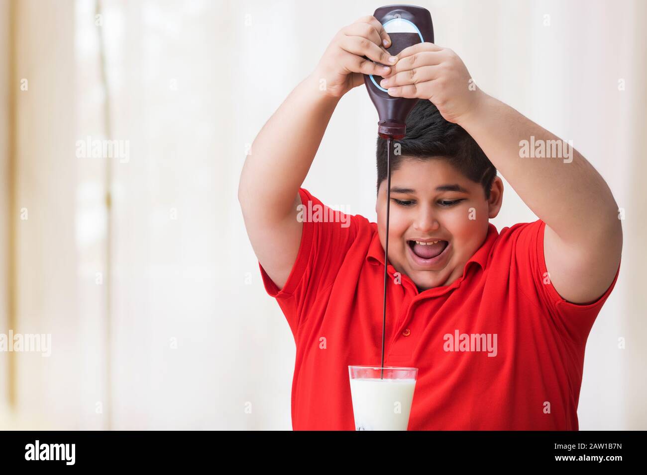 Young boy pouring chocolate syrup in the glass of milk. (Obesity) Stock Photo