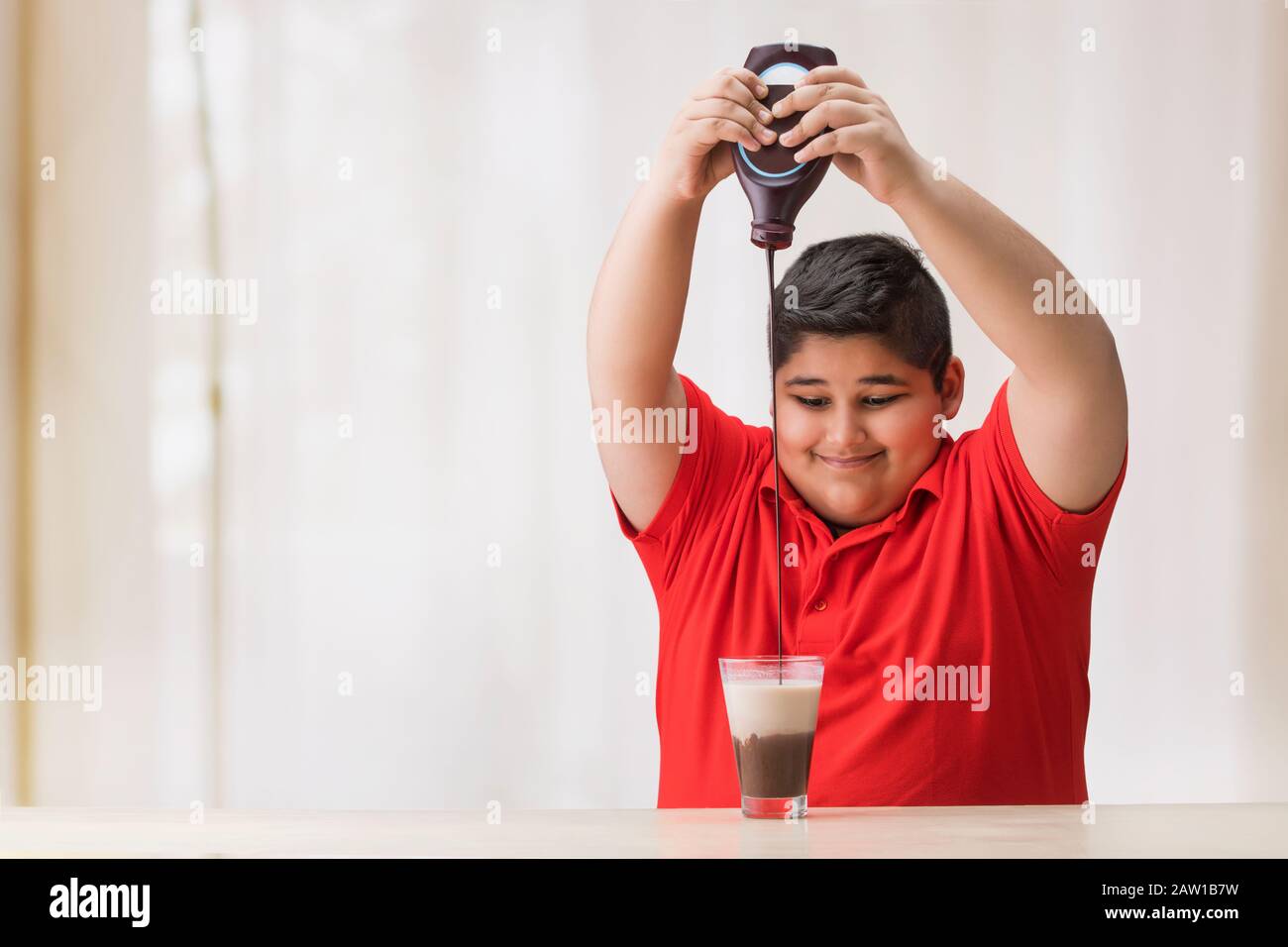 Young boy pouring chocolate syrup in the glass of milk. (Obesity) Stock Photo