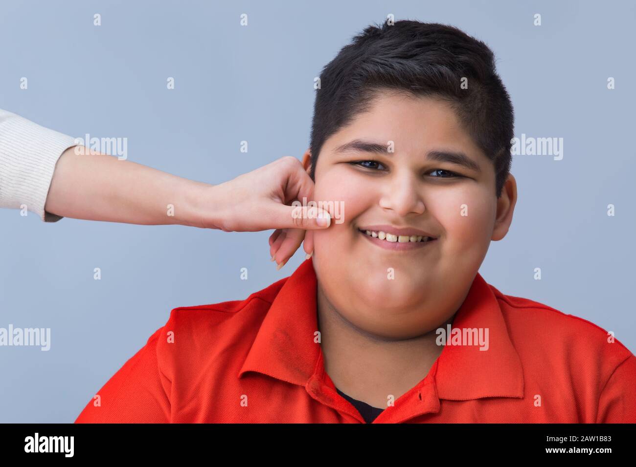 Young boy getting his chubby cheeks pulled. (Obesity) Stock Photo