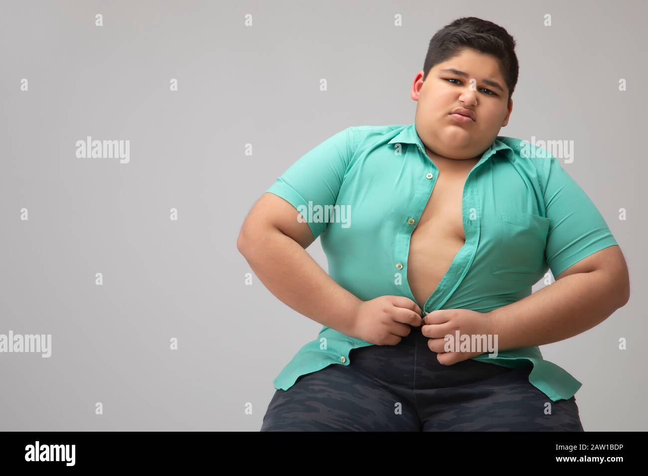 Young boy struggling to fit in a tight shirt. (Obesity) Stock Photo