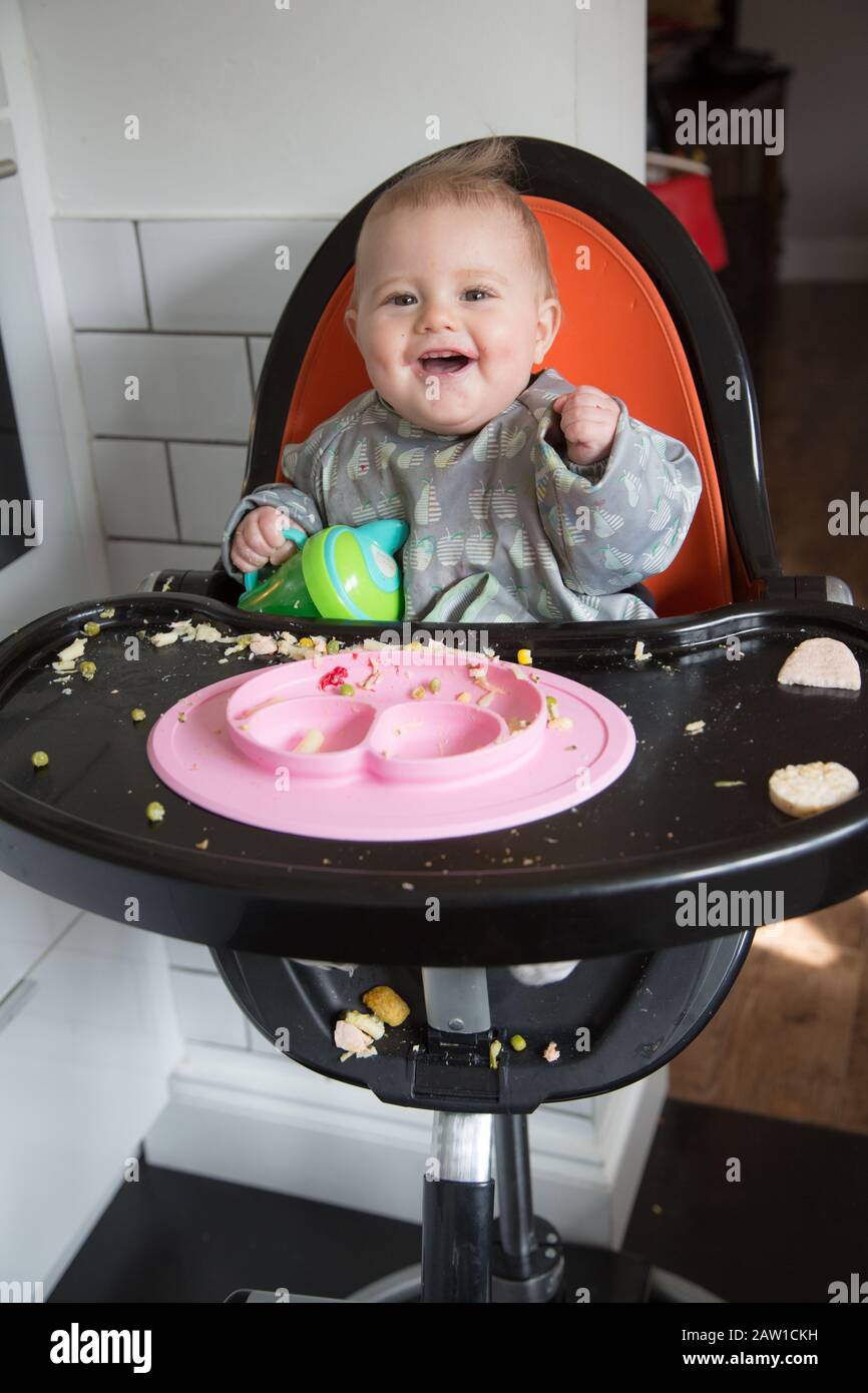 8-month-old-baby-girl-making-a-mess-eating-in-a-highchair-uk-stock