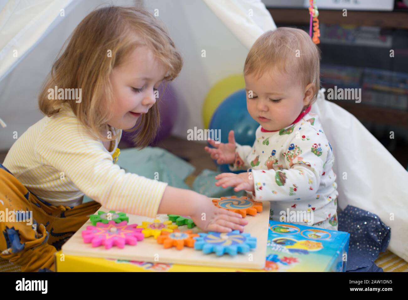 Siblings sitting in a tepee indoors opening presents, UK Stock Photo