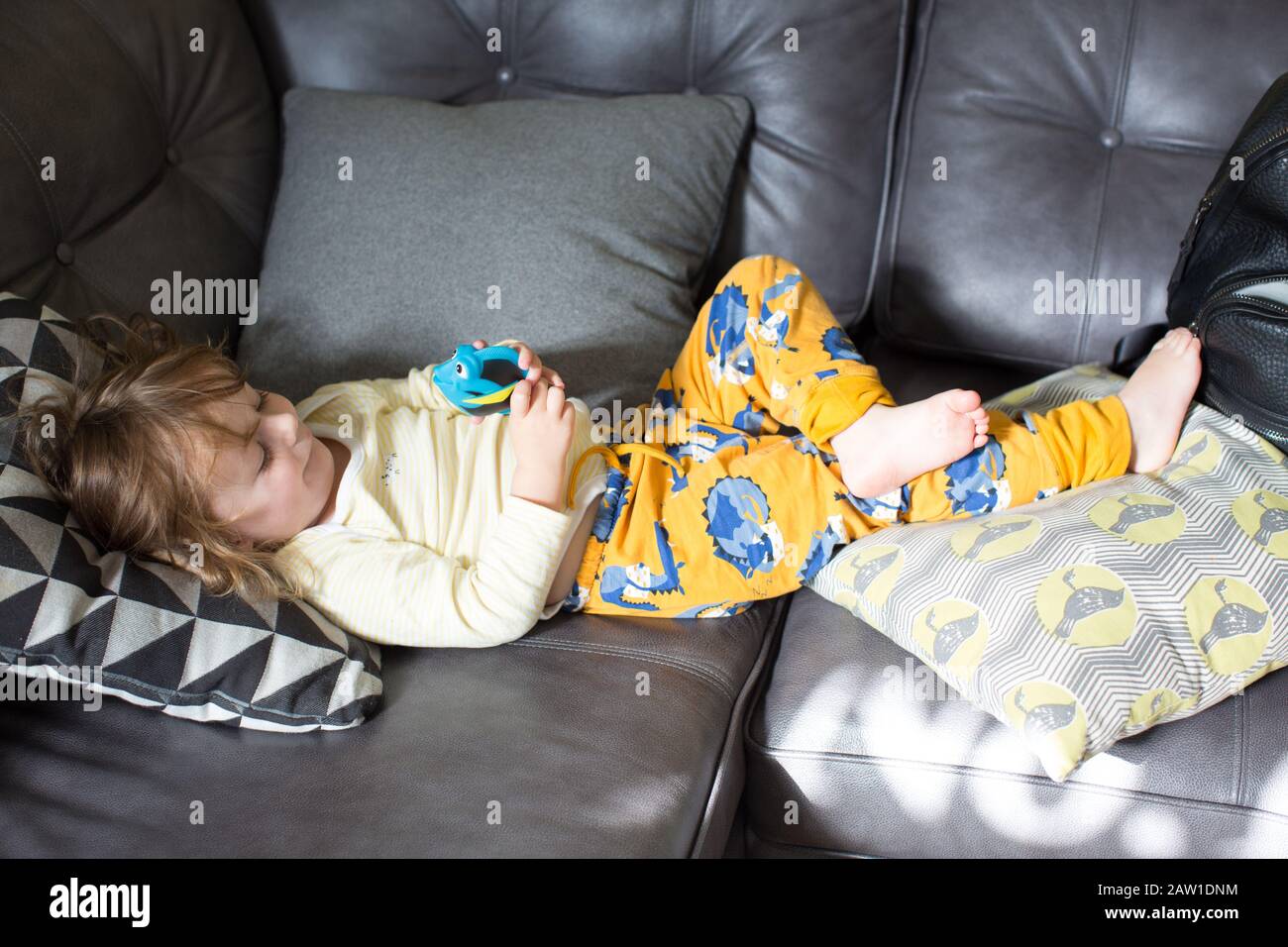 A toddler girl lying on the sofa in her pyjamas happily playing with a toy. UK Stock Photo