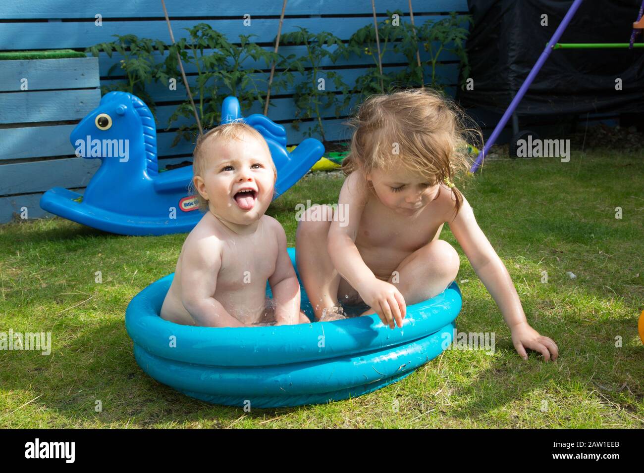 A baby and toddler sitting in a tiny paddling pool in their garden, U.K Stock Photo