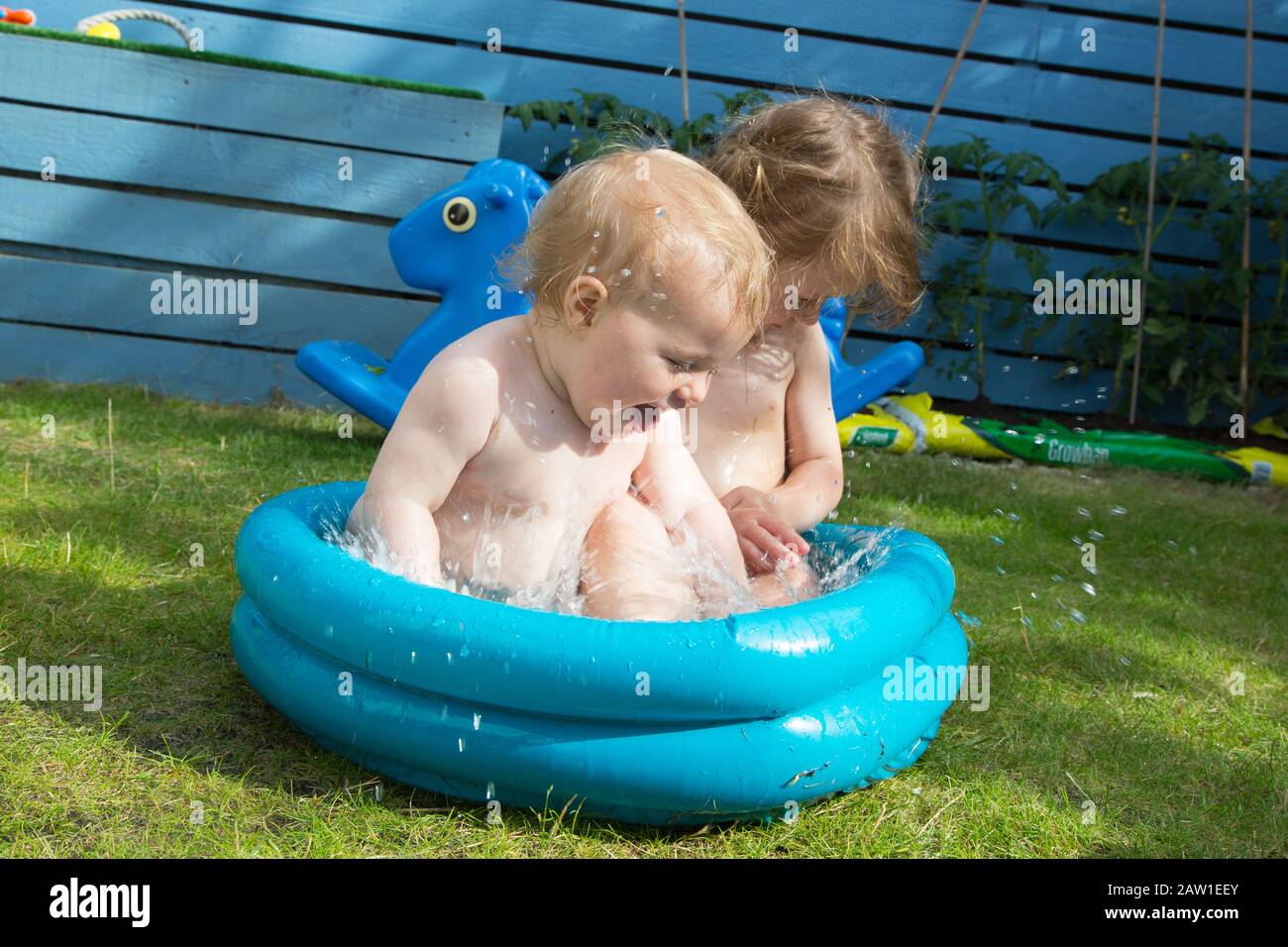 A baby and toddler sitting in a tiny paddling pool in their garden, U.K Stock Photo