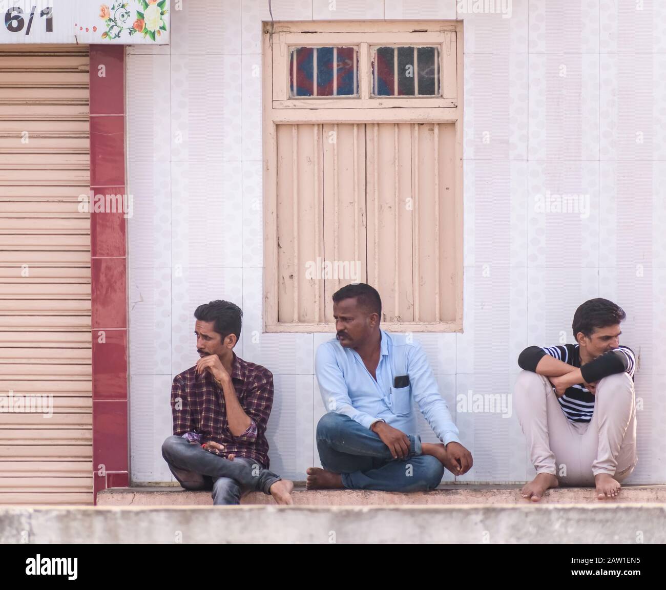 Diu, India - December 2018: Three men sit on a shelf outside the shuttered window of a shop on the streets of Diu. Stock Photo