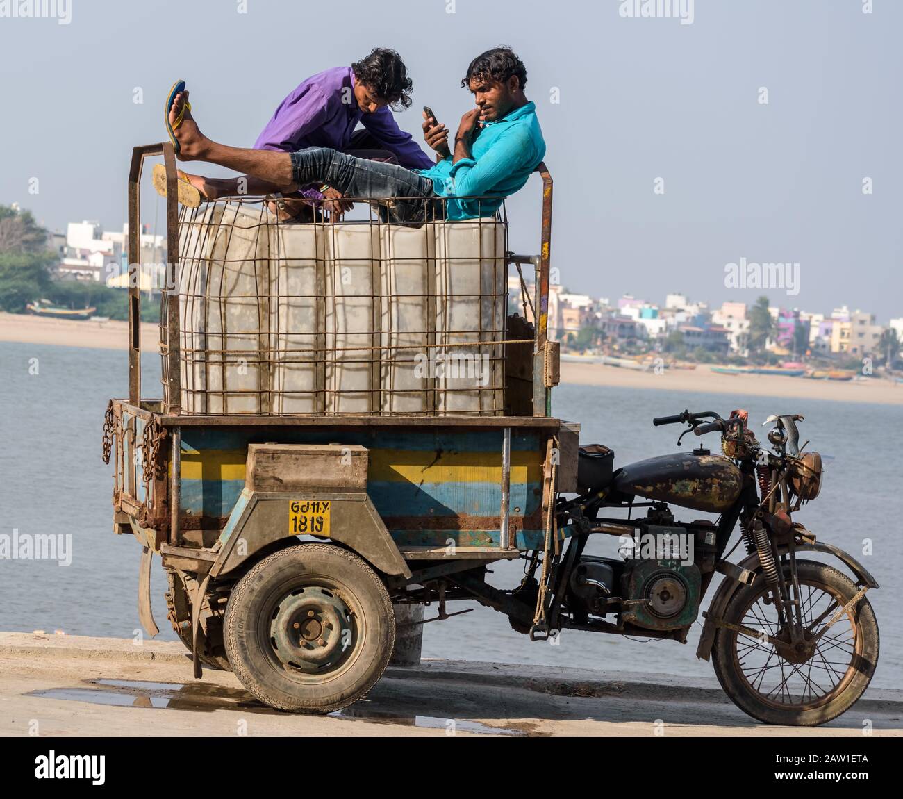 Diu, India - December 2018: Two fishermen relax on top of ice boxes loaded on a three wheeler vehicle by a pier on the island of Diu. Stock Photo