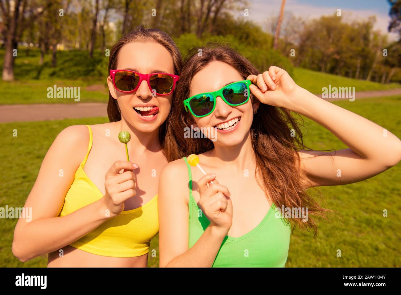 Attractive cheerful smiling girls having walk in park with lollipops Stock Photo