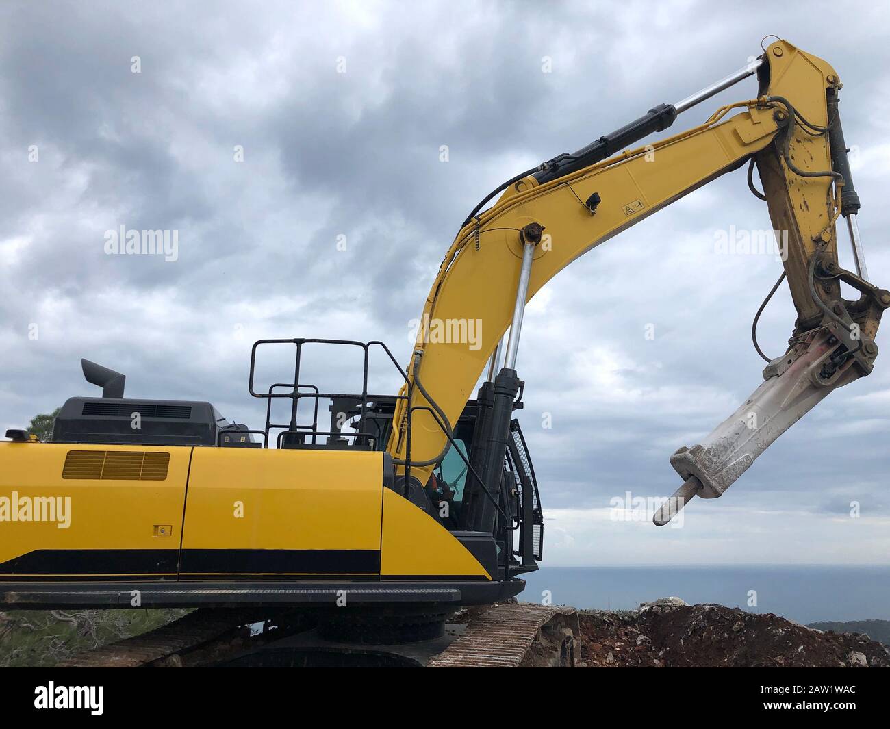 Hydrohammer during road construction works on the rocky soils. Heavy machinery at earthmoving, digging, excavation operations. Stock Photo