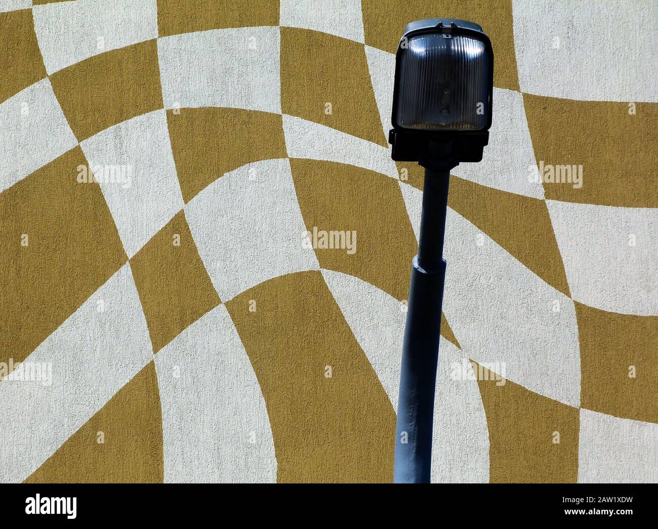 stucco building elevation detail. checkered pattern in white and mustard colors in Vasarely style. halogen street light head in front. low angle view Stock Photo