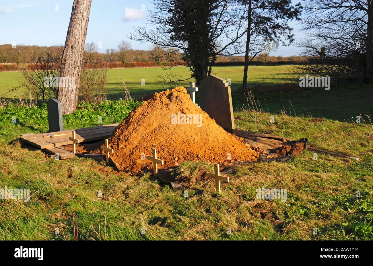 A grave dug and prepared for a burial in the corner of an English country churchyard. Stock Photo