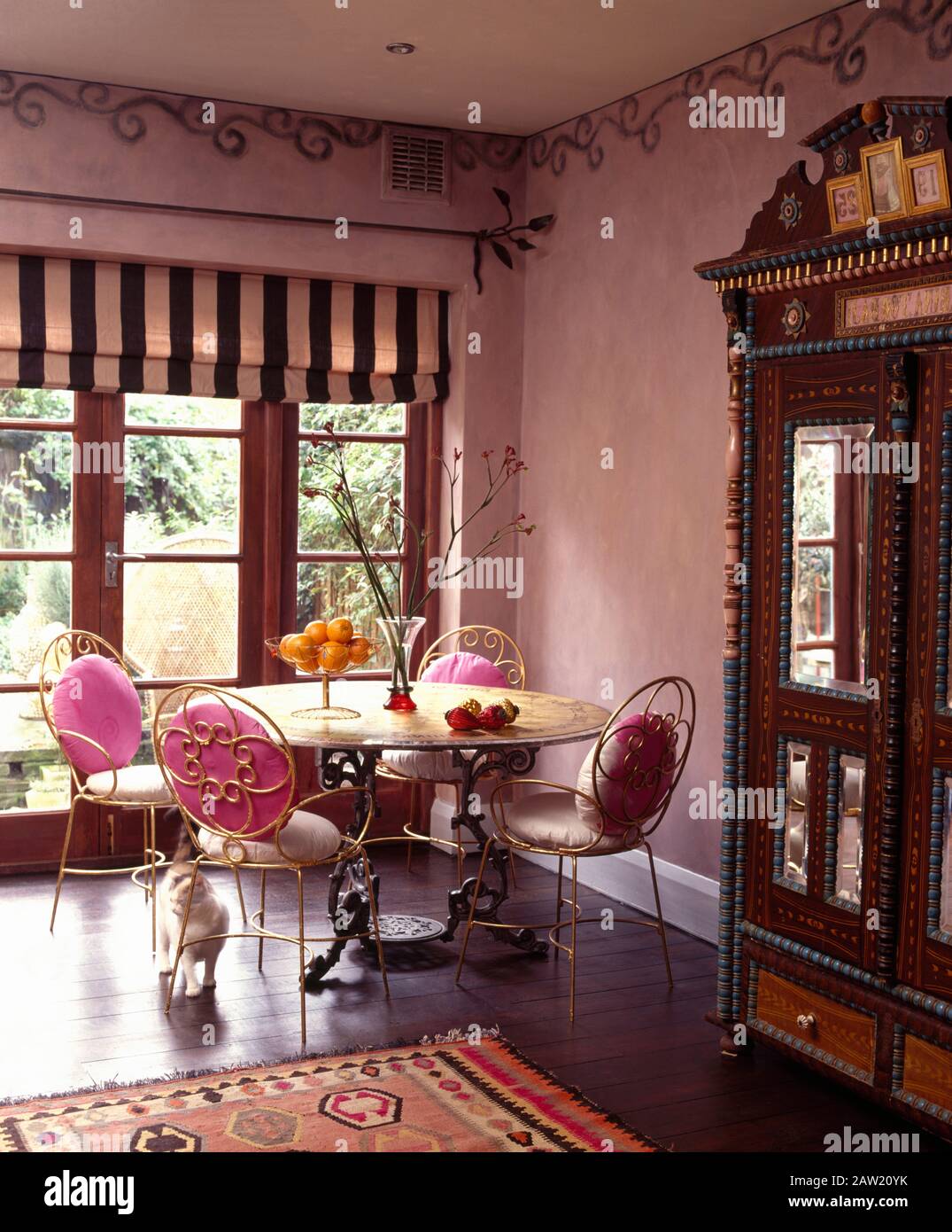 Gilt Metal Chairs At Ornate Wrought Iron Table In Dining Room With A Striped Blind On French Windows And Stenciled Border On The Wall Stock Photo Alamy