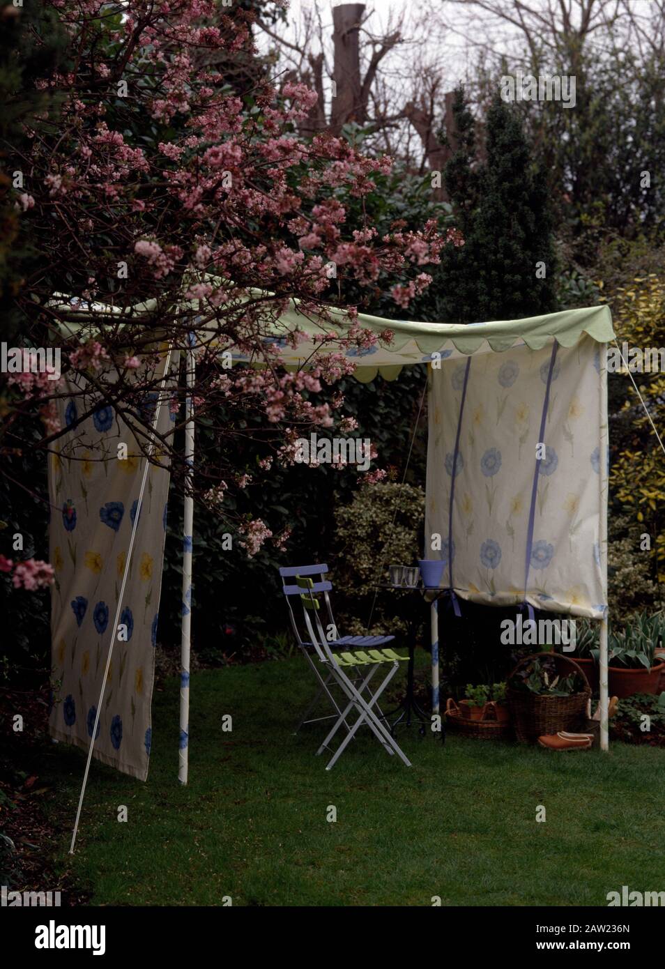 Colourful folding chairs under a home made fabric awning in a summer garden with pink roses