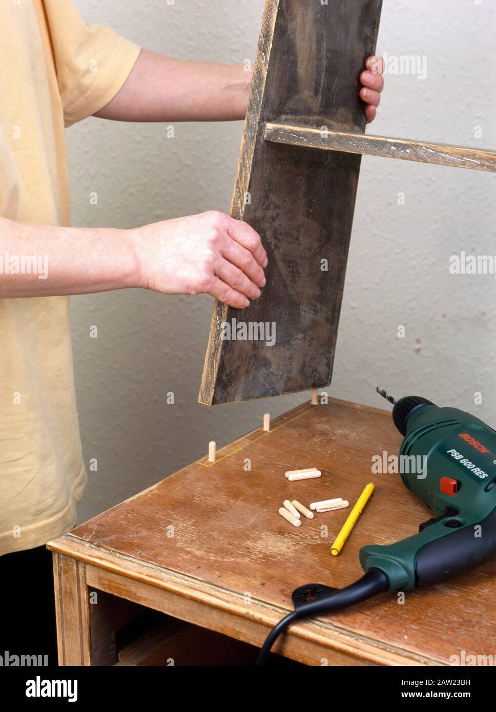 Craftsman using wooden dowels to attach shelves to a small chest of drawers to make a dresser Stock Photo