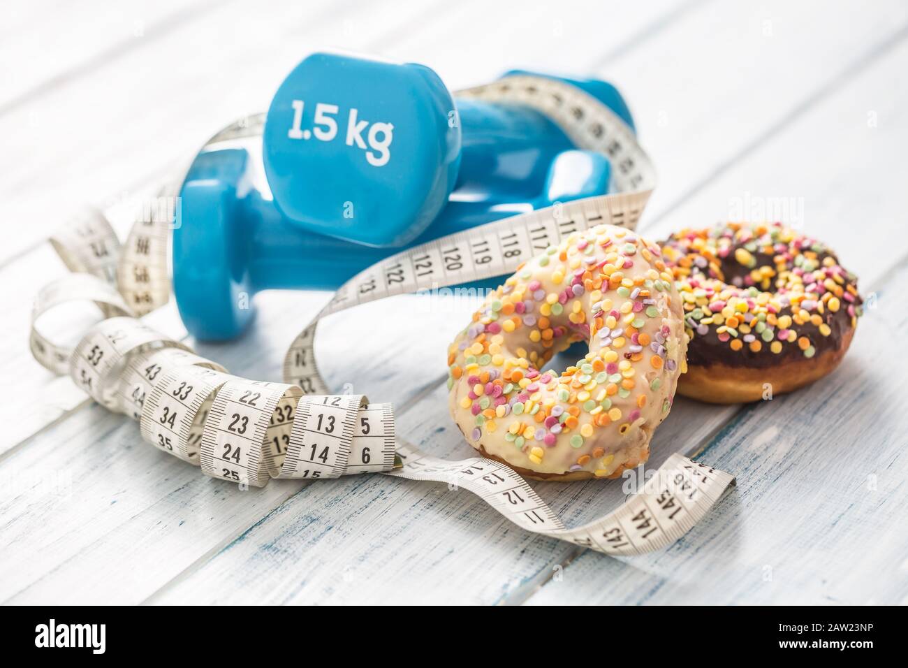 Sweet glazed donuts with dumbbells and measure tape on table. Stock Photo