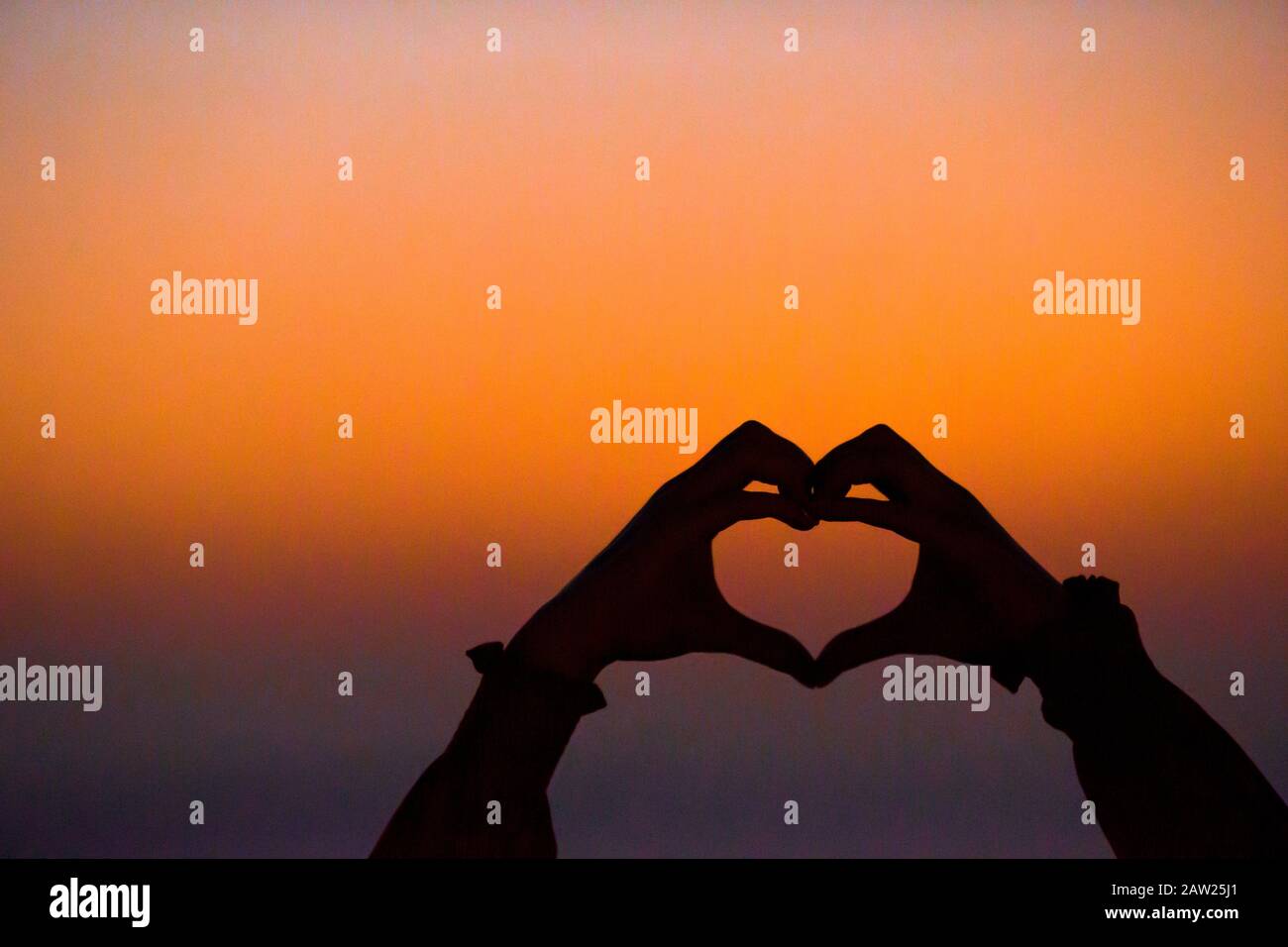 Silhouette of heart made by kids hand at sunset Stock Photo