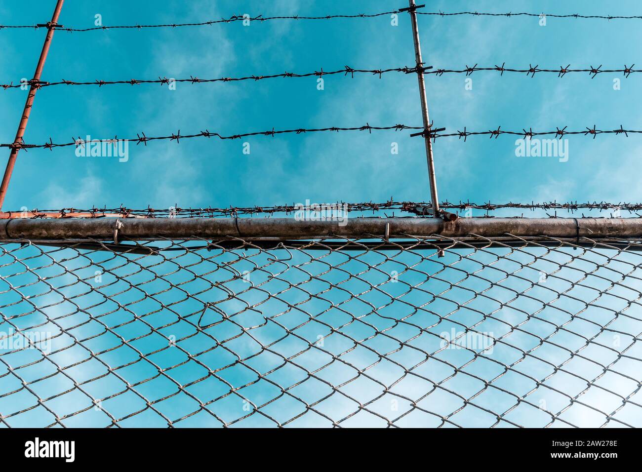 Metal fence with barbed wire and blue sky Stock Photo - Alamy