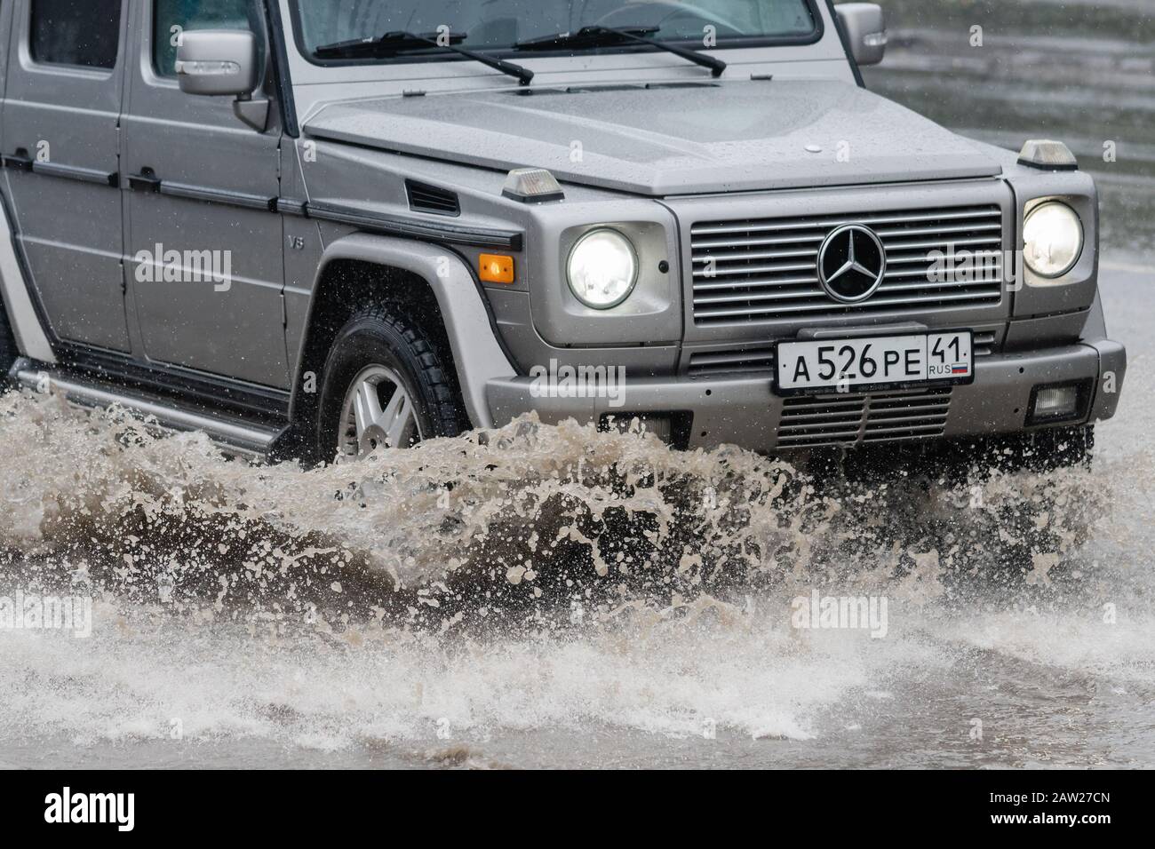 Mercedes-Benz G-Class, G-Wagen driving on flooded street road over deep muddy puddle and splashing drop of spray water from wheels Stock Photo