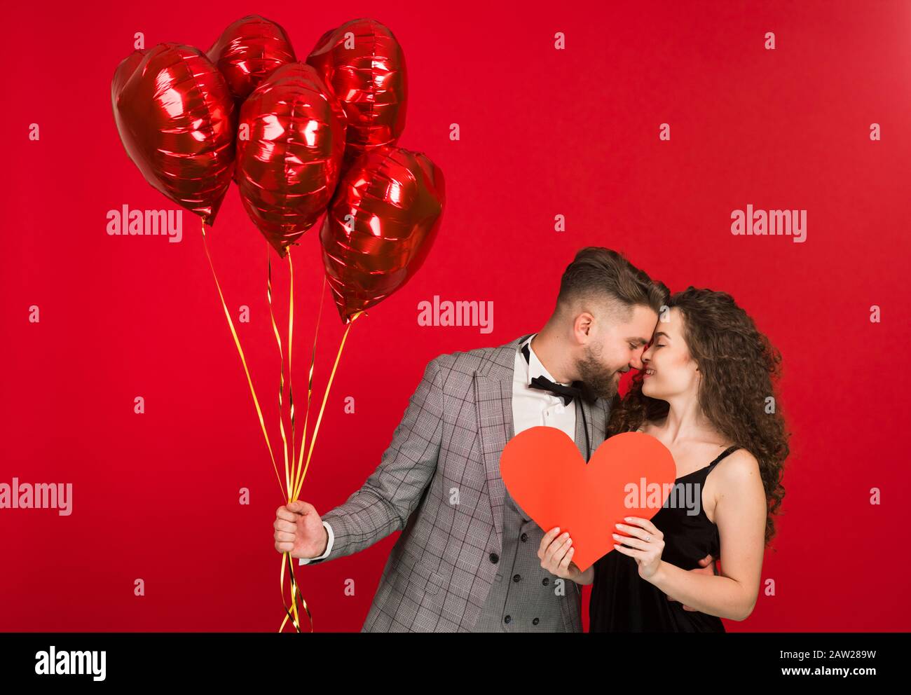 Joyful couple with heart shaped balloons isolated on red background ...