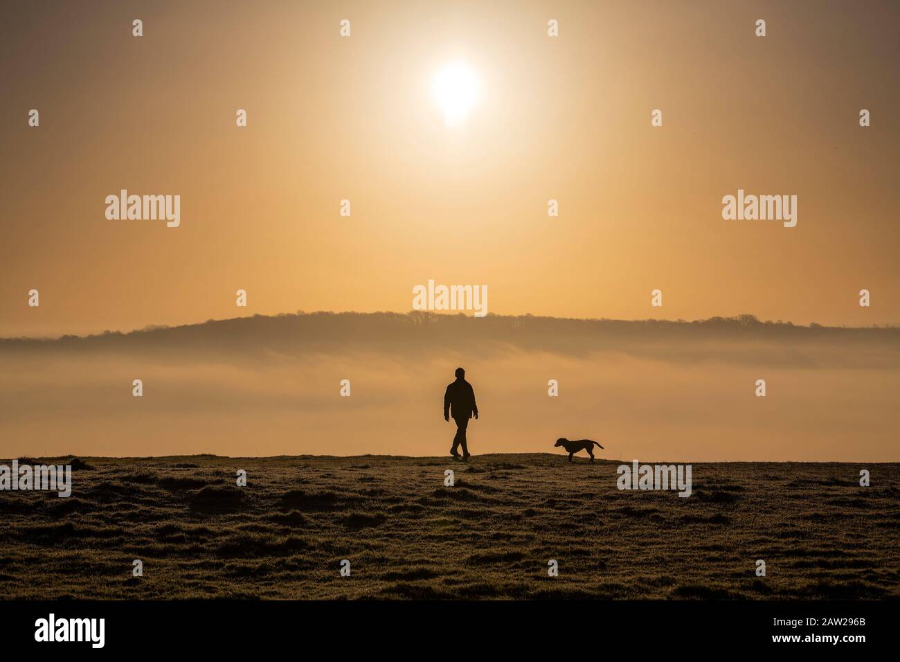 A man walks his dog at sunrise on Solsbury Hill near the City of Bath in Somerset, England. Stock Photo