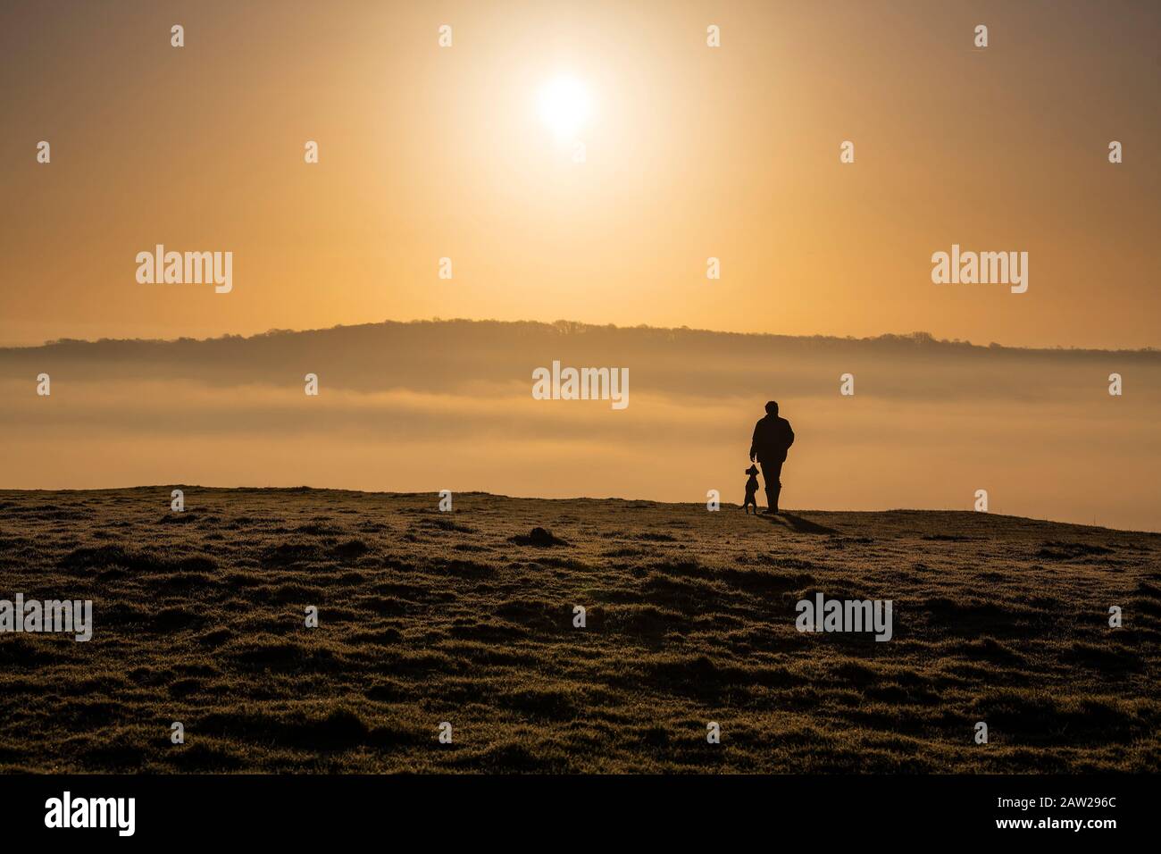 A man walks his dog at sunrise on Solsbury Hill near the City of Bath in Somerset, England. Stock Photo